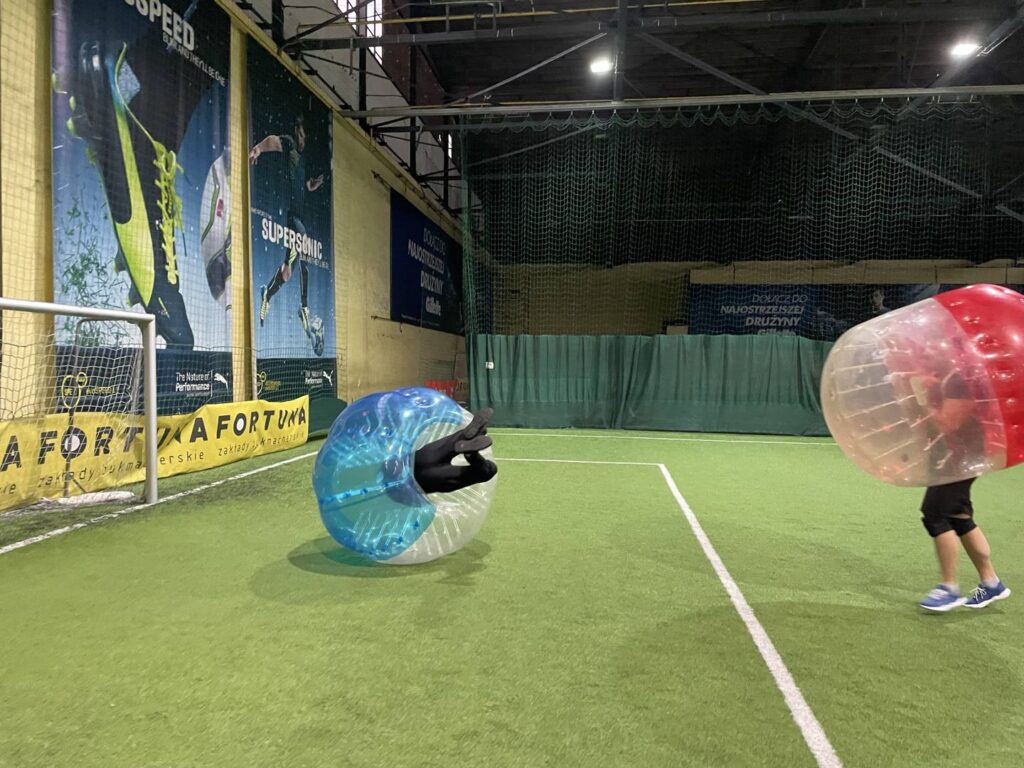 A player in a blue bubble upside down by the goal during bubble football in a sports hall