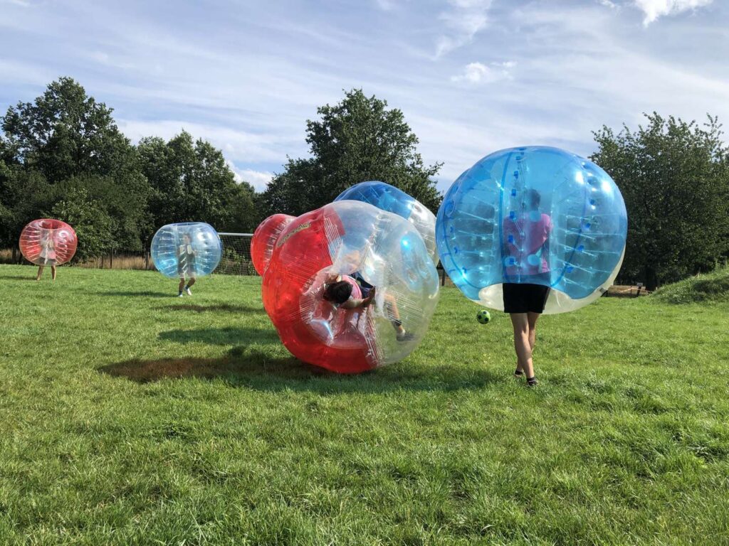 Mecz bubble football na trawie: gracz w czerwonej kuli przewraca się, obok zawodnik w niebieskiej kuli